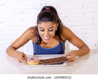 Young Attractive Latin Woman Sitting At Table About To Eat Chocolate And Doughnuts Looking Excited And Happy In No More Diet, Sugar And Chunky Unhealthy Food Concept.