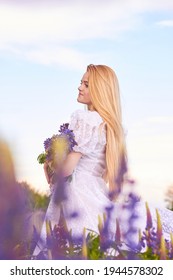 
Young attractive long  haired blonde in white vintage dress and bouquet lupins among purple field  The concept nature   romance 