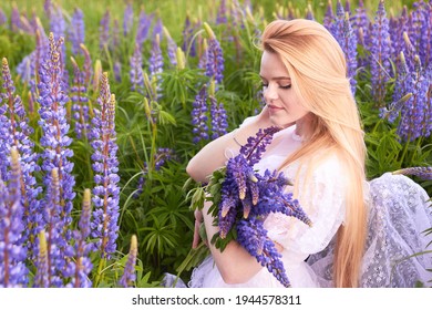 
Young attractive long  haired blonde in white vintage dress and bouquet lupins among purple field  The concept nature   romance 