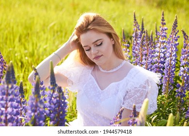 
Young attractive long  haired blonde in white vintage dress among purple field lupins  The concept nature   romance 