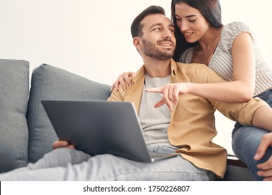 Young attractive lovely man and woman spending leisure time together and sitting on couch while using laptop