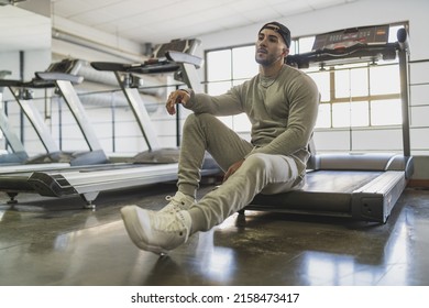 A Young Attractive Male In A Sweat Suit Posing Sitting On A Treadmill