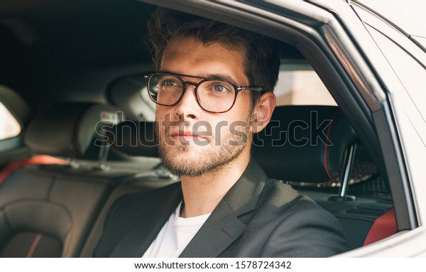 Young and attractive man with a beard and\
glasses smiles inside a car.\
Business
