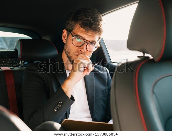 Young and attractive man\
with a beard and glasses works and looks at camera inside a car.\
Business
