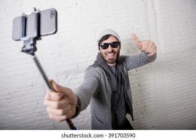 Young Attractive Man In Casual Clothes Beanie Hipster Style Holding Selfie Stick Mobile Phone Shooting Self Portrait Photo Or Recording Video In Internet Blog And Blogger Concept