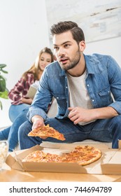 Young Attractive Man Holding A Slice Of Pizza While Watching Tv