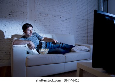 Young Attractive Man At Home Lying On Couch At Living Room Watching Tv Holding Remote Control And Changing Channel Or Volume Looking Interested And Excited With Comedy Movie Or Sitcom