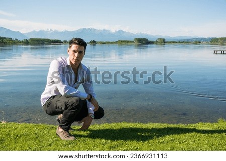 A young attractive man kneeling down next to a body of water. Photo of a man kneeling by the water's edge