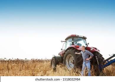 Young attractive man near a tractor. Tractor driver. Concept of agriculture and field works.