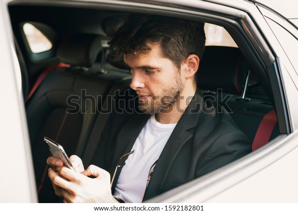 Young and attractive man uses\
his smartphone in a vehicle he does not drive. Businessfix\
spelling