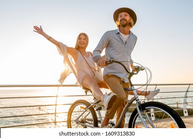 young attractive man and woman traveling on bicycles, romantic couple on summer vacation by the sea on sunset, boho hipster style outfit, friends having fun together