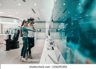 Young Attractive Multicultural Couple Looking For New Plasma Tv In Tech Store. Couple Hugging And Woman Pointing At Tv She Like.