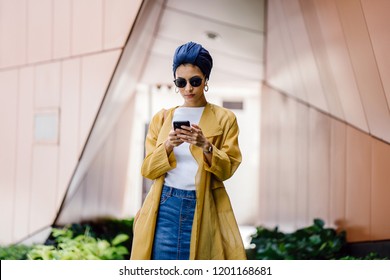 A Young And Attractive Muslim Malay Woman Wearing A Stylish Outfit, Turban (hijab, Head Scarf) And Sunglasses Is Streaming And Listening To Music On Her Phone. She Is Listening Via Wireless Earphones.