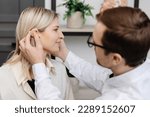 A young attractive otolaryngologist doctor gives a consultation to a female patient. A doctor explains how to wear a hearing aid to a woman.