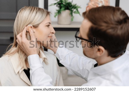 A young attractive otolaryngologist doctor gives a consultation to a female patient. A doctor explains how to wear a hearing aid to a woman.