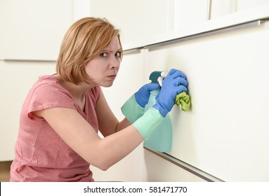 young attractive red hair woman or housewife leaning on kitchen with rubber  washing gloves cloth detergent cleaning bored and tired in stress of domestic housework concept