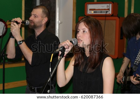 A young and attractive rock group soloist at a concert sings into a microphone. Underground music and informal atmosphere. Long-haired beautiful singer hugs a microphone. Gentle voiced female voice
