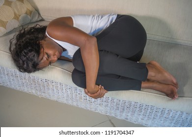 Young Attractive And Sad Black African American Woman Lying In Fetal Position Depressed At Home Sofa Couch Suffering Menstruation Period Pain And Belly Cramps Feeling Anxious And Frustrated