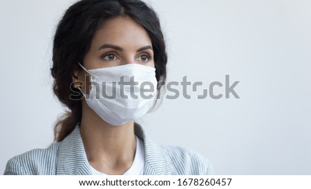 Young attractive serious woman in protective facial medical mask posing over blue background with copy space for text. Coronavirus COVID19 pandemic infection outbreak prevention, personal care concept
