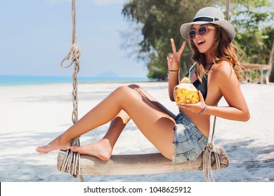 Young Attractive Sexy Woman On Vacation Sitting On Swing By Sea, Tropical Beach, Drinking Cocktail In Coconut, Skinny Legs, Traveling In Thailand, Smiling, Happy, Positive Emotion, Summer Style