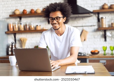 Young attractive smiling African American casually dressed entrepreneur working from home using his laptop computer. Freelance, remote work, distant education concept. - Powered by Shutterstock