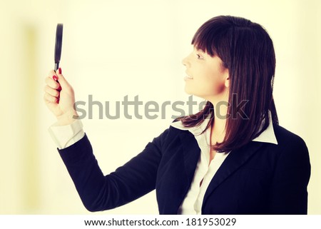 Young attractive smiling business woman looking into a magnifying glass