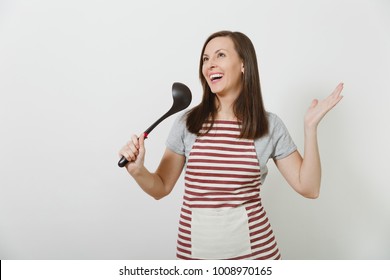 Young attractive smiling caucasian housewife in striped apron isolated on white background. Beautiful housekeeper woman sings into kitchen soup ladle like microphone. Copy space for advertisement