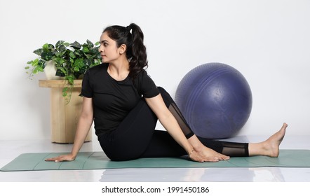Young attractive smiling woman practicing yoga, wearing sportswear, pants and top, indoor full length at home