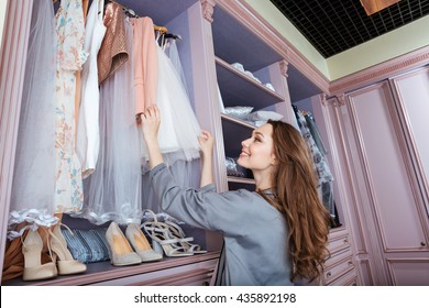 Young attractive smiling woman searching what to wear in a wardrobe