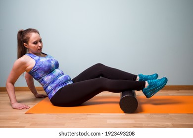 Young Attractive And Sportive Woman Rolling Foam Roll By Legs To Perform Sensory Stimulation And To Ease Muscular Tension. Self Myofascial Release With Foam Roll. Excercising At Home.