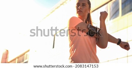 Young attractive sporty girl warming up outdoors, doing stretching in city