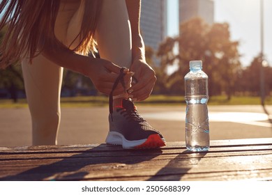 Young attractive sporty woman making pause for tying shoelaces and drink water during exercising in the park. - Powered by Shutterstock