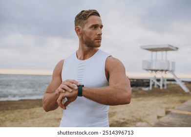 Young attractive strong sporty athletic toned fit sportsman man wear sports clothes look at smartwatch warm up training at sunrise sun dawn over sea beach outdoor on pier seaside in summer day morning - Powered by Shutterstock