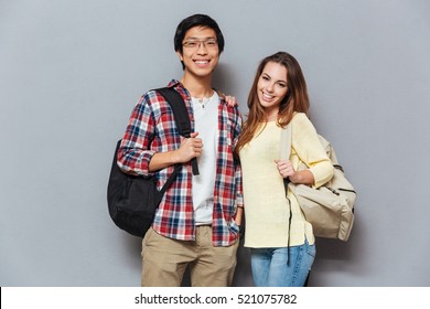Young attractive students couple standing together with backpacks isolated on the gray background