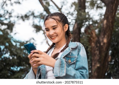 A young attractive teenager chats on her phone with her boyfriend. Having a fun, casual conversation. Nature park background.