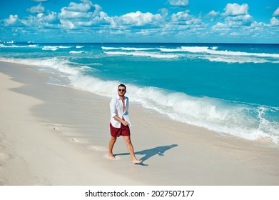 Young Attractive Tourist Male In White Shirt And Sunglasses Walking Alone On The Cancun Beach, Mexico. Travel, Vacation Concept. Man 