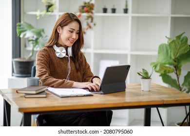 Young Attractive University Student Using A Laptop Computer, Studying Online At Home. Cheerful Caucasian Asian Woman Writes Notes, Planning Working Process, Sitting At Home. Exam Preparation. 