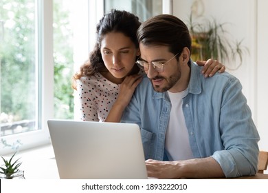 Young Attractive Wife Hugging Husband Wearing Glasses From Back, Looking At Laptop Screen Together, Using Computer, Spouses Surfing Internet, Shopping Online, Making Purchases, Booking Tickets