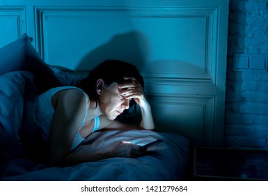 Young attractive woman awake late at night using smart phone lying in bed in a dark bedroom. Using mobile for chatting and sending messages in internet addiction, mobile abuse and insomnia concept - Shutterstock ID 1421279684