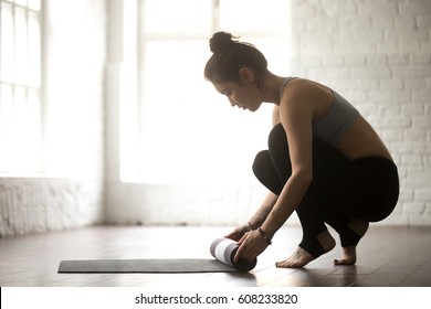 Young attractive woman before or after practicing yoga, preparing for exercise, unrolling or rolling yoga mat, wearing sportswear bra and pants, full length, white loft studio background - Powered by Shutterstock