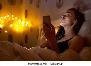 Young, attractive woman before bed listening and enjoying relaxing music after a hard, working day. Chatting online with friends - Powered by Shutterstock