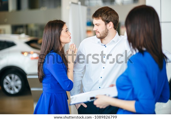 Young attractive woman begging her boyfriend\
to buy a car in\
auutosalon
