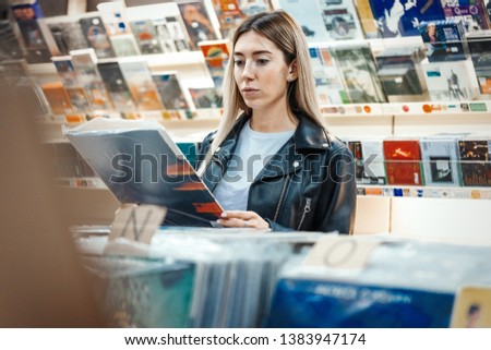 Young attractive woman choosing vinyl record in music record shop. Melomaniac or music addict concept.