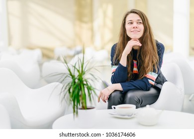 Young Attractive Woman With A Cup Of Tea In A Cafe.  Smiling, Gap Teeth. Bright Modern Interior. Natural Unconventional Beauty. Communication With Riends, Conversation, Talk. Looks At The Camera