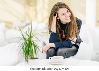 Young Attractive Woman With A Cup Of Tea In A Cafe.  Smiling, Gap Teeth. Bright Modern Interior. Natural Unconventional Beauty. Communication With Riends. Looking Away