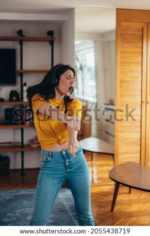 Young attractive woman dancing while listening a music on a headphones at home