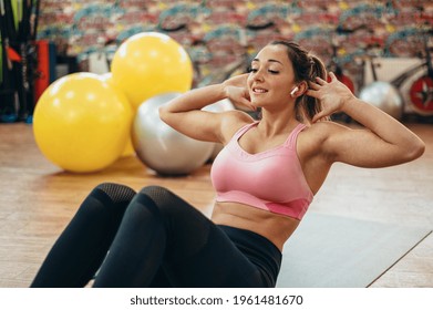Young attractive woman doing crunchers in the gym while using airpods