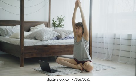 Young Attractive Woman Doing Yoga Exercise And Watching Tutorial Lesson On Laptop Computer At Home