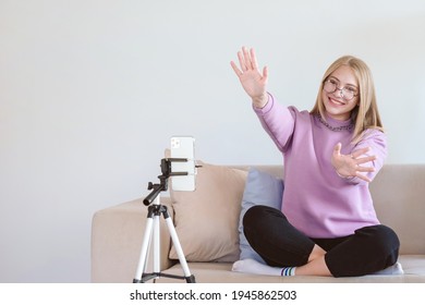 Young attractive woman greeting followers. Blogger or vlogger recording video on mobile phone at home and making content for internet. Human on white background with text place.