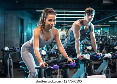Young attractive woman and handsome man  doing cardio workout cycling bikes in the gym